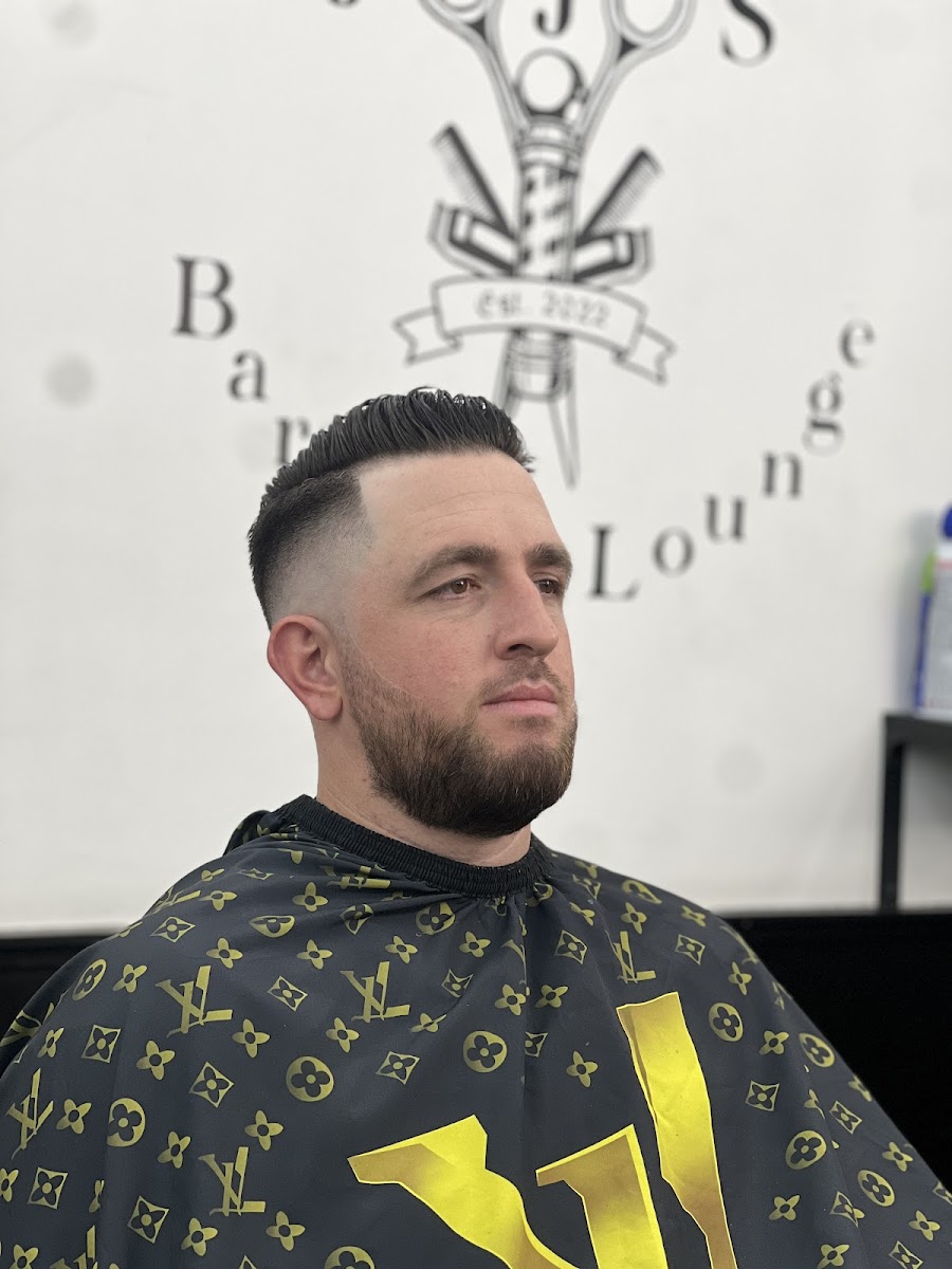 Side profile of a clean fade with full beard, in front of the Jojo's logo