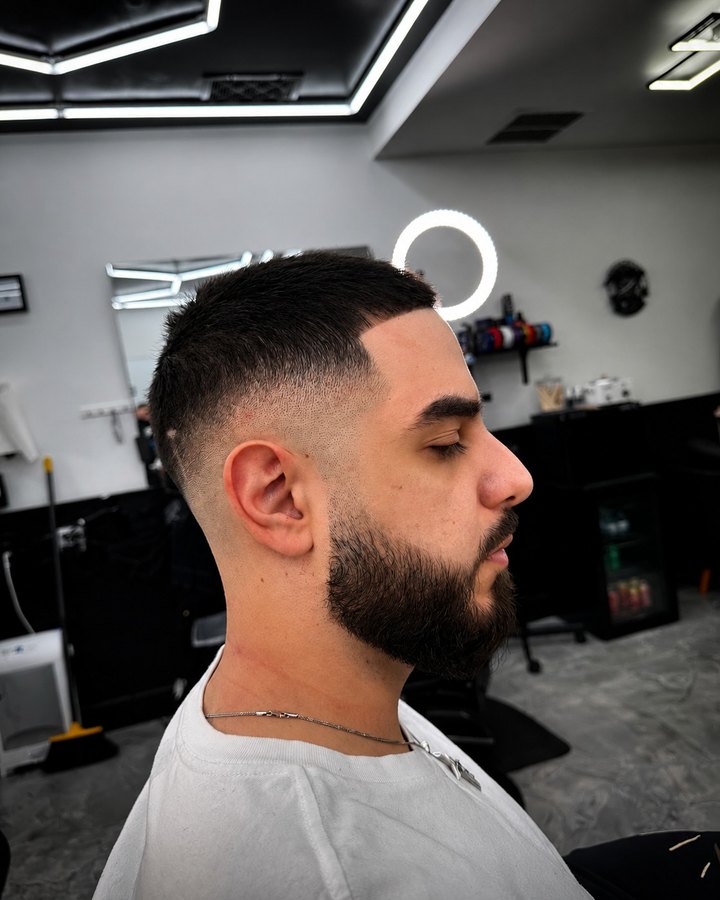 Skin fade with full beard, hex ceiling visible behind