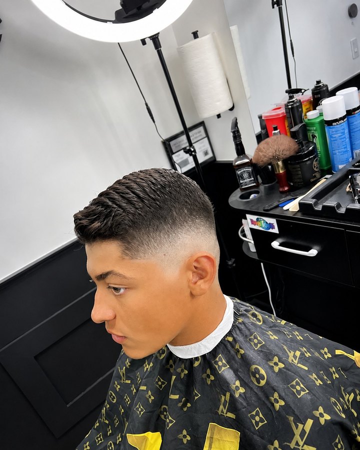 Classic side-part with skin fade, LV cape with ring light and workstation behind