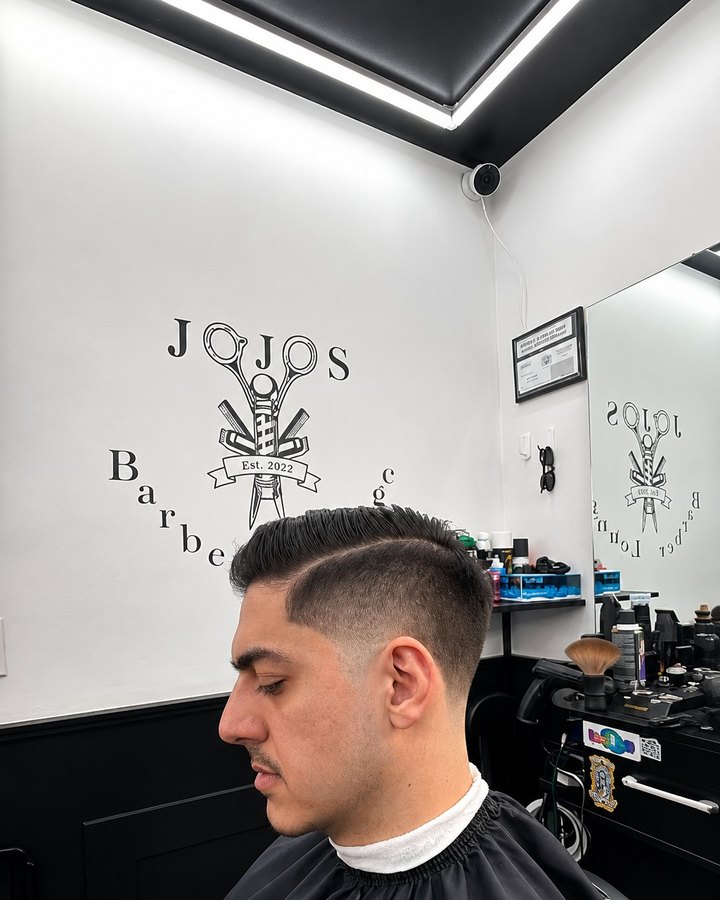 Side profile of a fresh skin fade in front of the Jojo's Barber Lounge wall logo